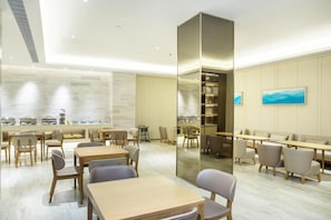 A modern dining area with wooden tables and chairs, a central column, and a view of the kitchen through a glass partition. - Ji Hotel Shanghai New Jiangwan City Yingao Road (Shanghai)