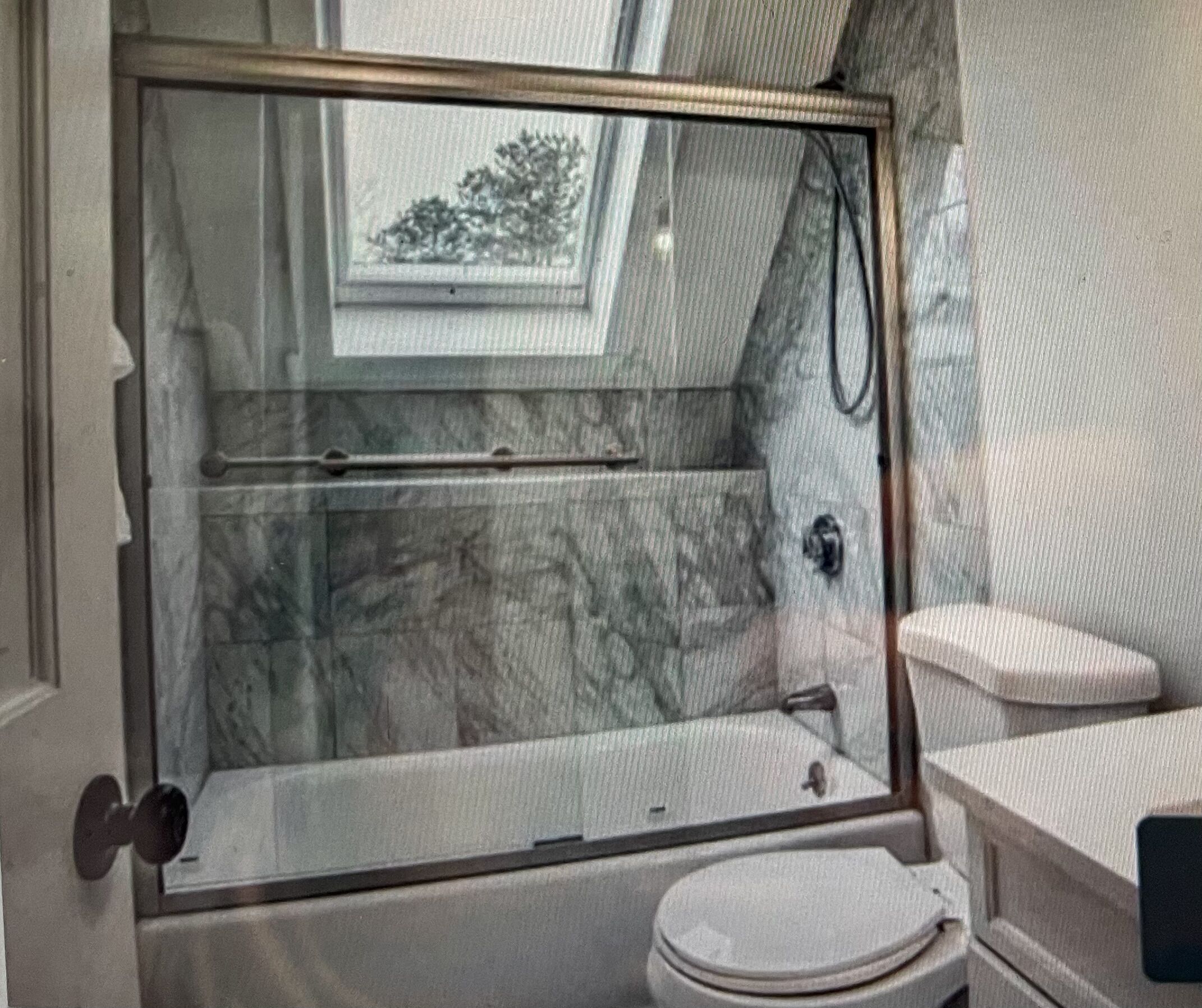 Une salle de bain avec une douche à parois de verre, des toilettes et un mur en marbre.