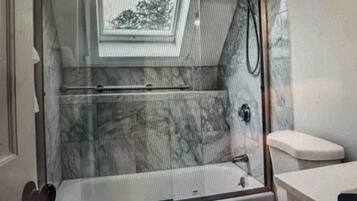 Een badkamer met een douchecabine van glas, een toilet en een marmeren wand.