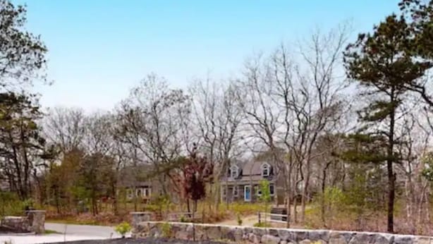Un quartier résidentiel avec une pelouse bien entretenue, un mur de soutènement en pierre et une maison à deux étages dotée d’une porte bleue.