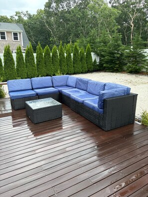 Une terrasse en bois avec un canapé d’angle bleu et un pouf assorti.