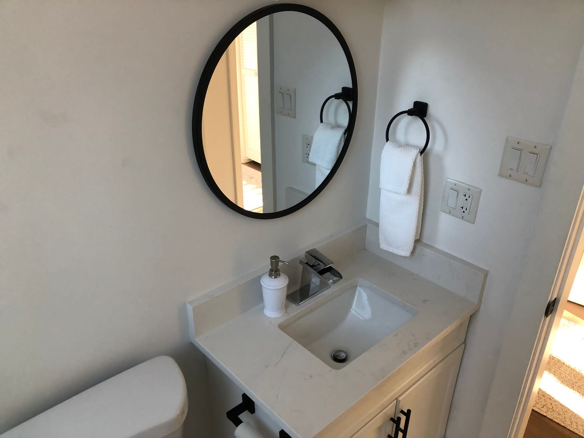 Un baño con un espejo redondo, un lavabo, un inodoro y un perchero para toallas.