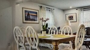 Un coin repas avec une table ronde, des chaises blanches, une plante en pot et des tableaux encadrés accrochés aux murs.