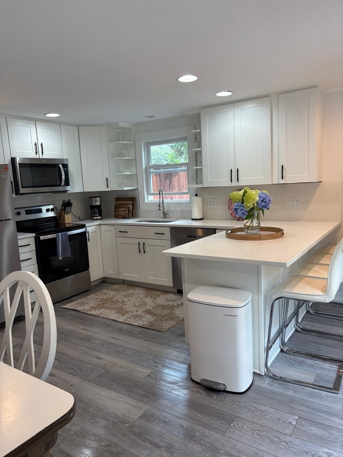 A modern kitchen with white cabinetry, a built-in microwave, an oven, and a sink. There's a small island with a vase of flowers.