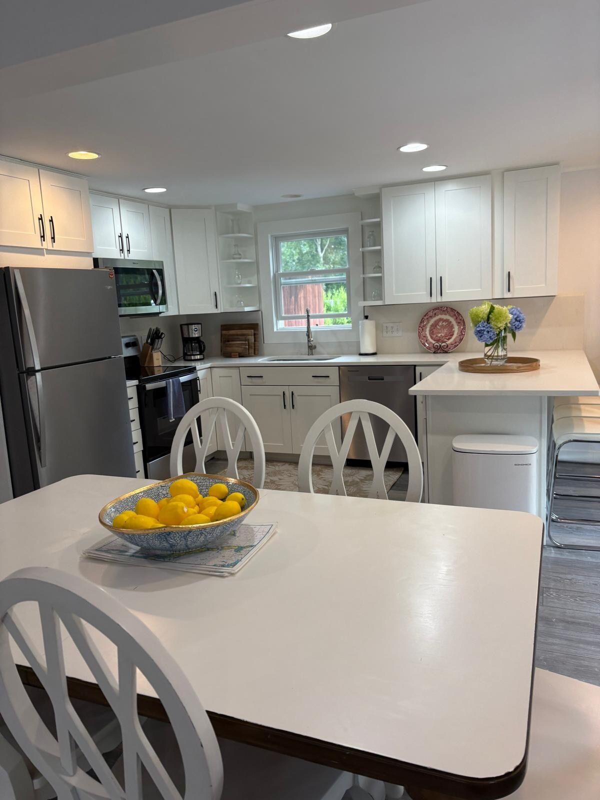 A modern kitchen with white cabinetry, a stainless steel refrigerator, a microwave, and a dining area with a white table and chairs.