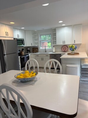 Une cuisine moderne avec des meubles blancs, un réfrigérateur en acier inoxydable, un four à micro-ondes et un coin repas comprenant une table et des chaises blanches.