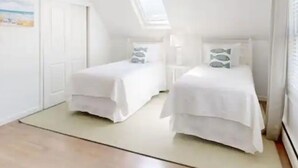 Une chambre avec deux lits, une lucarne et une porte.