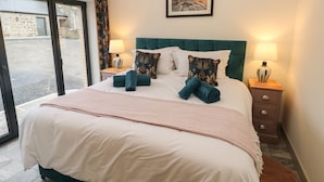 A neatly made bed with a teal headboard, two bedside tables with lamps, and a large window with curtains.