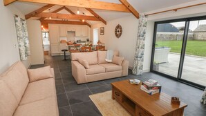 A spacious living area with a sofa, a wooden coffee table, and a view of the kitchen and outdoor patio. - The Byre (Bridgend)