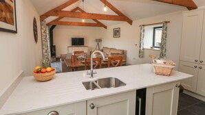 A kitchen with a white countertop, wooden beams, a sink, and a dining area with a table and chairs. - The Byre (Bridgend)