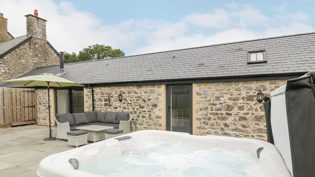 A stone building with a hot tub, outdoor seating, and a wooden door. - The Byre (Bridgend)