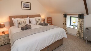Een slaapkamer met een groot bed, nachtkastje, kapstok, raam met gordijnen en een ingelijst schilderij aan de muur.
