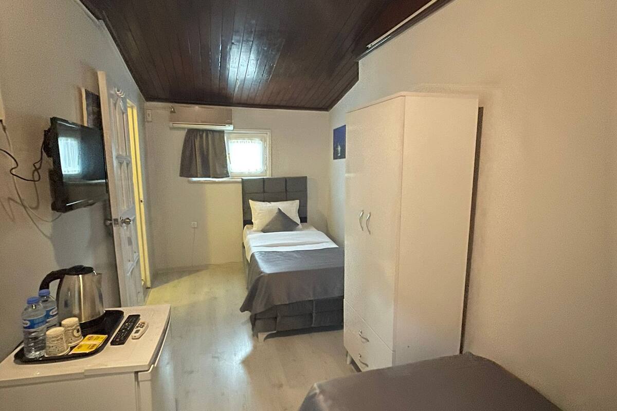 A compact room with a bed, a small desk with a kettle, a TV, and a wardrobe.