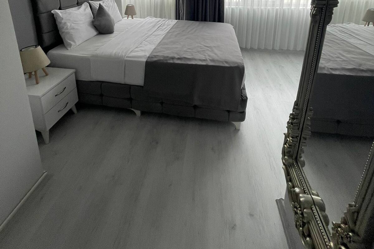A modern bedroom with a large bed, a nightstand, a mirror, and a painting on the wall.