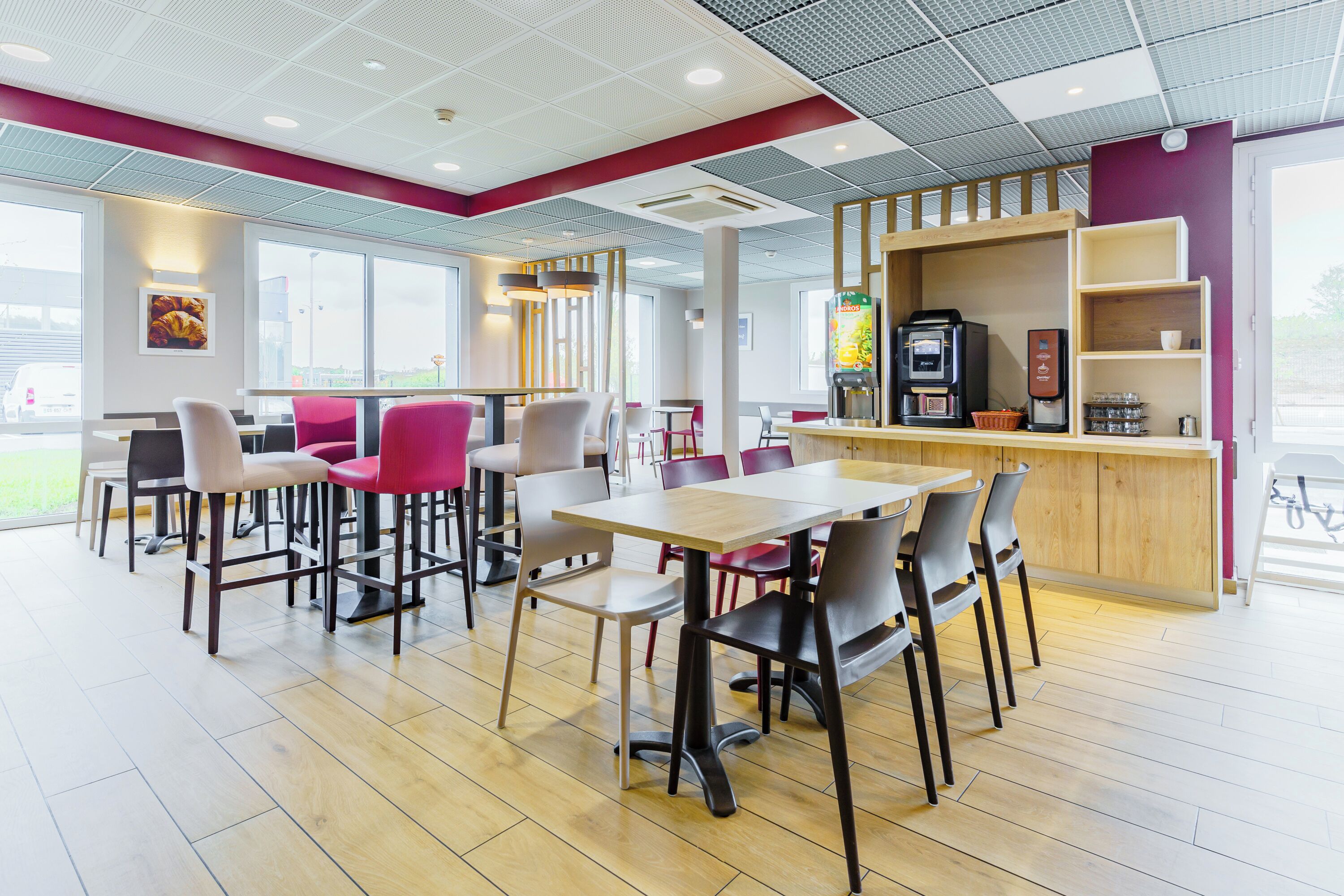 A modern cafe with wooden tables and chairs, a coffee machine, and a vending machine.