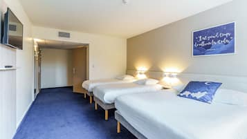 Habitación de hotel con tres camas individuales, un televisor y una frase inspiradora en la pared.