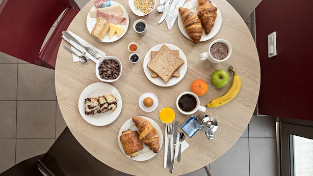 Una mesa redonda con alimentos para el desayuno, como cruasanes, pan, frutas y café.