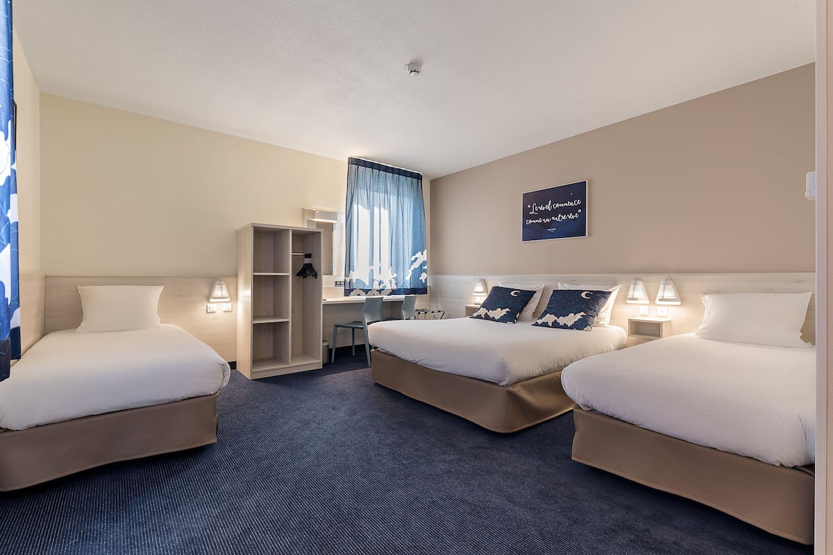 A hotel room with two beds, a desk, a chair, and a wardrobe.