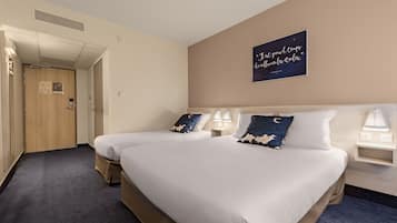 A hotel room with two beds, a nightstand with a lamp, a wall clock, and a sign with a quote.