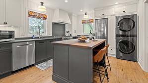 A modern kitchen with stainless steel appliances, a central island, and wooden flooring. - La Bella Rosa, Queen Street is your backyard! (Niagara-on-the-Lake)