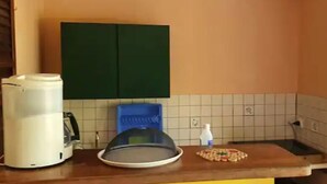 Una cocina con cafetera, un escurreplatos azul y una pequeña mesa con un plato.