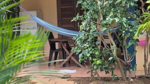 Una hamaca atada entre dos sillas de madera, una mesita pequeña y una planta en maceta en un jardín.
