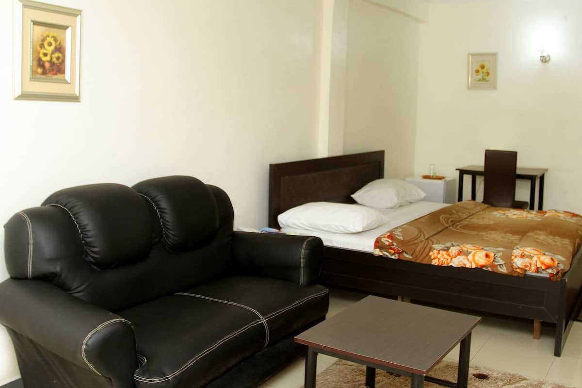 Un dormitorio con cama, sofá de cuero negro, una mesita y una puerta.