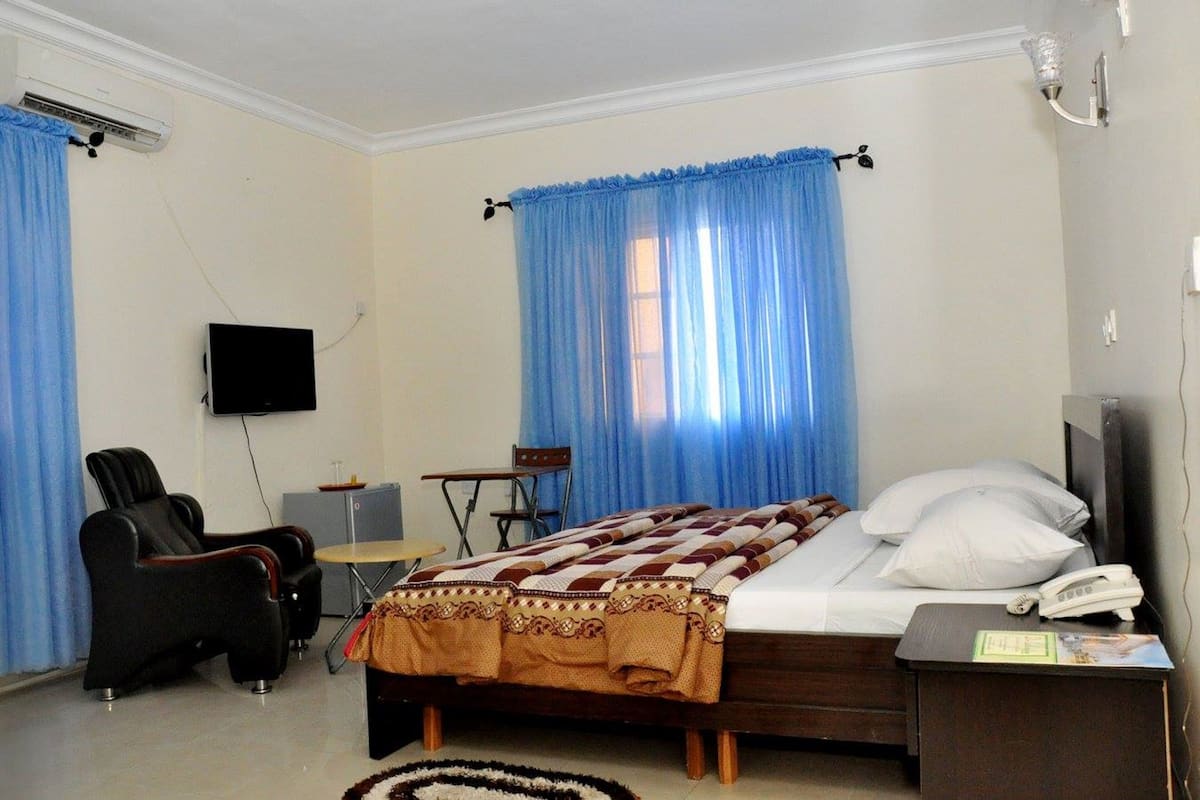 Habitación de hotel con cama, escritorio, silla, televisión y ventana con cortinas.