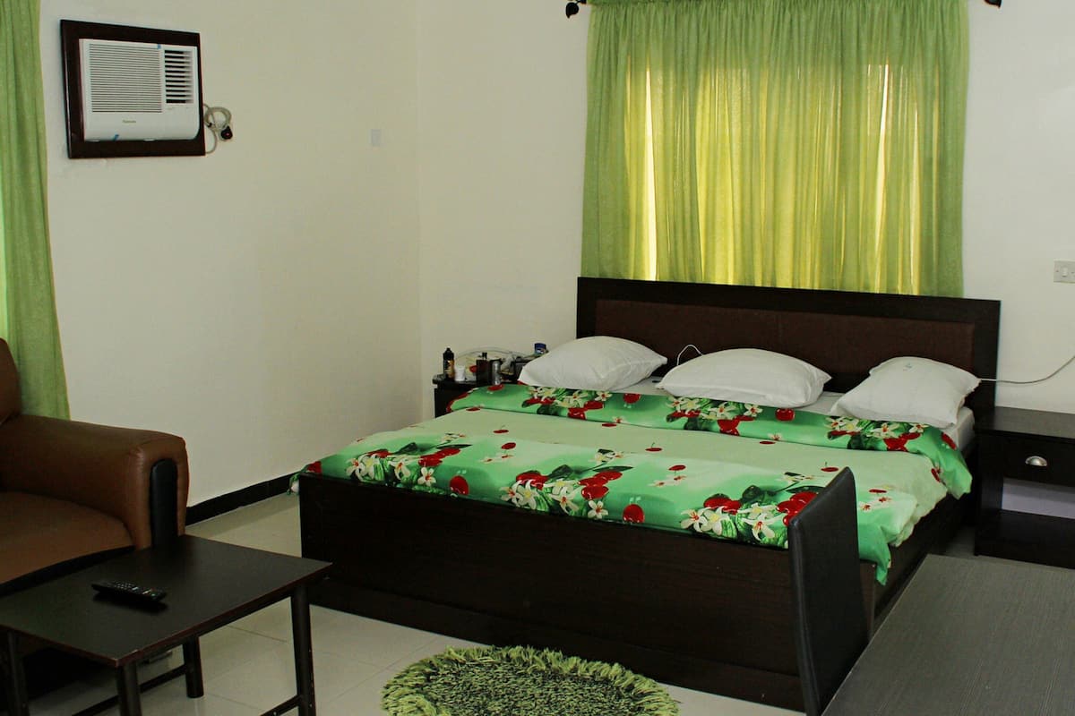 Un dormitorio con cama, una silla, una mesita de noche y una lámpara.