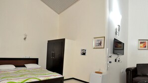Habitación de hotel con cama, escritorio, silla, televisor y cortina verde.