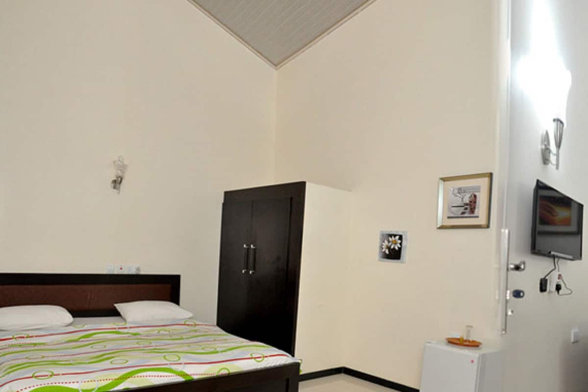 Habitación de hotel con cama, escritorio, silla, televisor y cortina verde.
