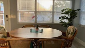 Un comedor con una mesa redonda, sillas de mimbre y una planta en maceta.