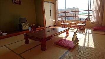 Una habitación japonesa tradicional con suelo de tatami, una mesa de madera baja y vistas a la ciudad a través de amplios ventanales.