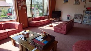 A living room with red sofas, a television, and a window with a view of the outside. - Nakanosawa Onsen Ryokan Shirokiya (Inawashiro)
