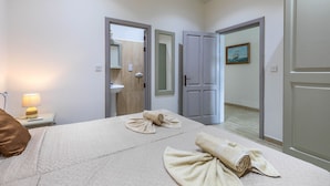 Habitació d'hotel amb llit, una vetustat amb una làmpada, un bany amb un rentapeus i una porta que dona a una altra habitació.