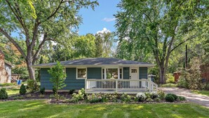 A single-story house with a front porch, surrounded by a well-maintained lawn and trees.