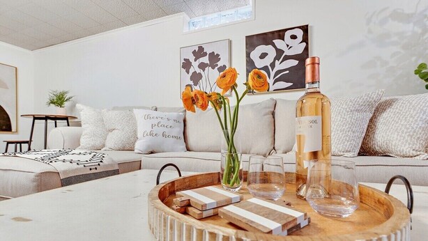 A modern living room with a sofa, a coffee table with a tray, a bottle of wine, and decorative flowers.