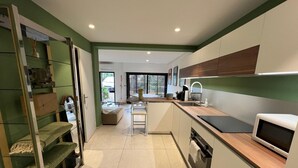 A modern kitchen with a central island, built-in appliances, and a sliding door leading to a dining area. - 2 CHAMBRES JARDIN/TERRASSE ACCES PLAGES A2B241 (Cannes)