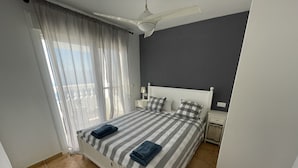 Een slaapkamer met een bed, gordijnen, een nachtkastje en een plafondventilator.
