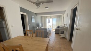 Een eetgedeelte met een houten tafel en stoelen, een plafondventilator en uitzicht op de woonkamer door een open deur.