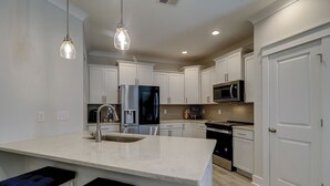 A modern kitchen with white cabinets, stainless steel appliances, and a marble countertop.