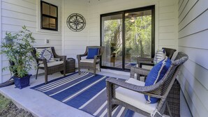 A covered porch with wicker furniture, a blue striped rug, and a potted plant.