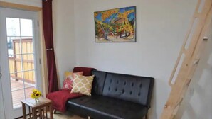 Una sala de estar con un sofá de color oscuro, una mesita de madera con un jarrón de flores y un cuadro en la pared.