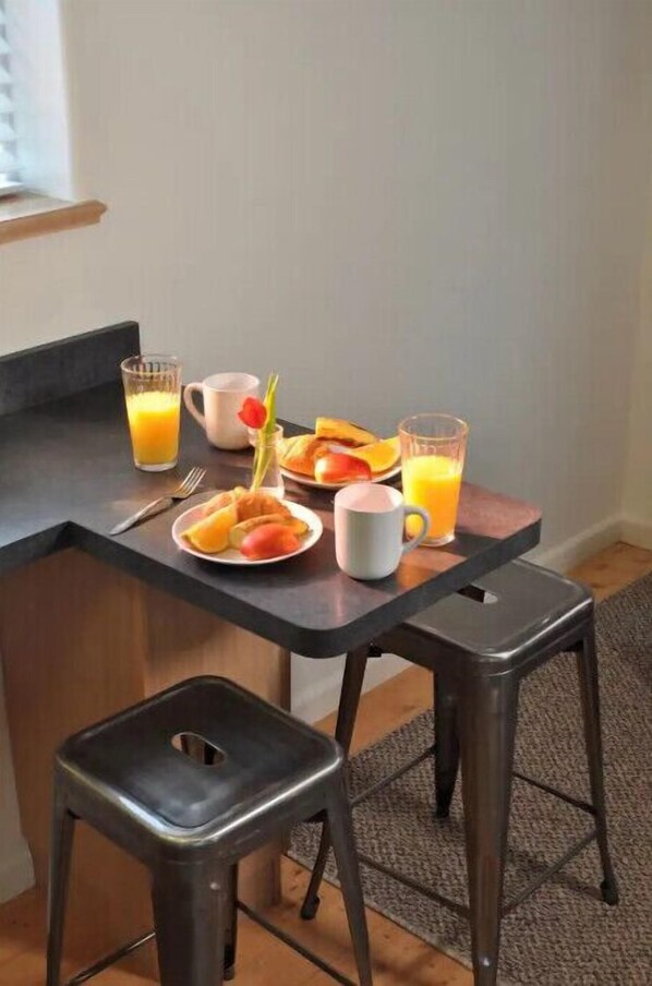 A breakfast setup with a table, two stools, a plate of fruit, a mug, and glasses of orange juice.