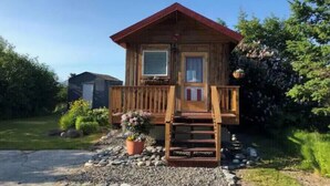 Una cabaña de madera con techo rojo, un porche delantero y un pequeño jardín con una maceta.