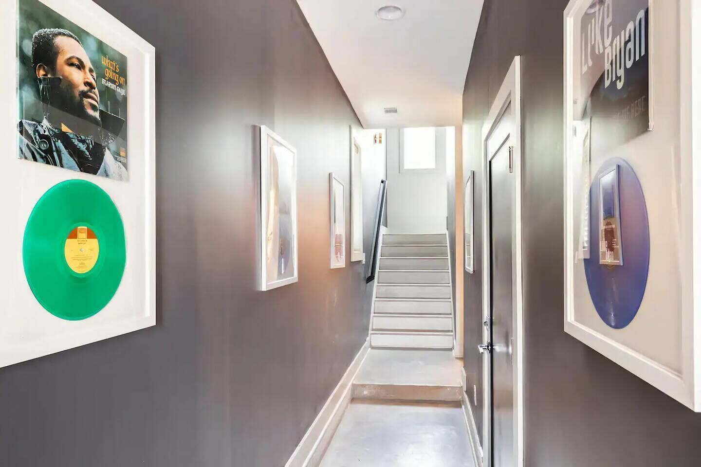 A hallway with framed artwork, a green vinyl record, and a staircase leading to another floor.