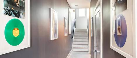 A hallway with framed artwork, a green vinyl record, and a staircase leading to another floor.