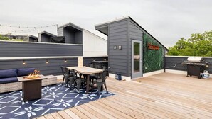Ein Außenbereich mit einer Holzterrasse, einem Feuerkorb, einem Esstisch mit Stühlen und einem Grill.