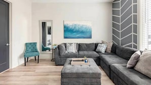 Ein modernes Wohnzimmer mit einem grauen Ecksofa, einem petrolfarbenen Sessel und einem Couchtisch.