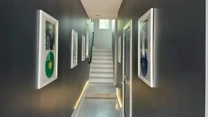 Ein Flur mit gerahmten Bildern an den Wänden, einer Wendeltreppe in der Mitte und einer Leuchte an der Decke.